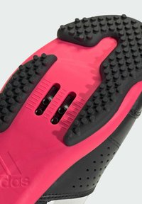 Nahaufnahme eines schwarzen und pinken Schuhs mit strukturiertem Grip und sichtbaren Schrauben zur Befestigung der Stollen an der Sohle eines Radschuhs.
