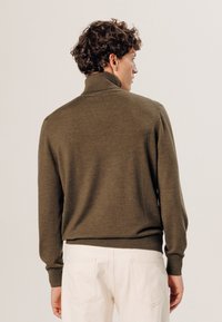 Pull vert en tricot avec un col montant, doté de manches longues et d'une taille ajustée. La texture semble douce et légère.