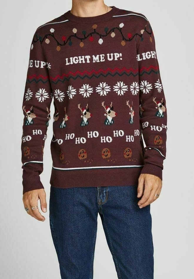 Pull marron avec des motifs festifs, incluant des rennes, des flocons de neige et des biscuits en pain d'épice. Présente le texte "LIGHT ME UP!" en crème.