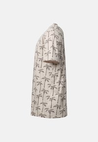 T-shirt beige à manches courtes avec un motif répétitif de palmiers noirs, présenté de côté sur un fond uni.