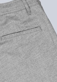 Nahaufnahme von grauen Stoffhosen, die die Details der hinteren Paspeltasche und des Gürtelschlaufs zeigen.