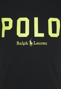 Czarna tkanina z dużym żółtym napisem "POLO" nad małym logo zawodnika polo i nazwą marki "Ralph Lauren" na żółto.