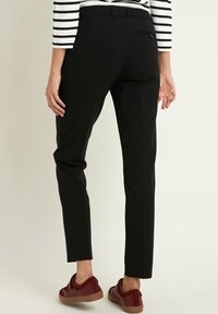 Černé přiléhavé kalhoty s hladkou texturou, zúženými nohavicemi a detailním zadním kapsou, v kombinaci s bordó pohodlnými botami.