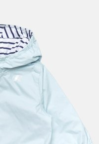 Giacca a vento blu chiaro con cappuccio foderato a righe bianche e navy. Presenta un dettaglio logo discreto sul davanti. Realizzata in materiale liscio e resistente all'acqua.