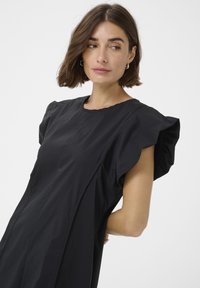 Črna obleka s kratkimi, nabranimi rokavi, okroglo izrezom in gladko teksturo; ima vertikalne šive za strukturirano zasnovo.