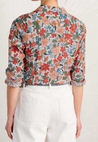 Camicia a bottoni floreale in tessuto leggero, con fiori multicolori in rosso, arancione e blu su uno sfondo grigio chiaro.