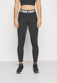 Black athletic leggings with a fitted design, branded waistband, and subtle seam detailing. Paired with dark running shoes.