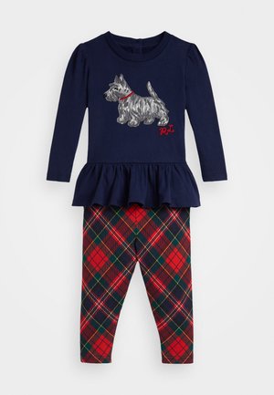 Marineblå langermet topp med plisserte kanter, prydet med en sølvfarget hund-embroidery og røde detaljer, kombinert med røde og grønne rutete leggings.