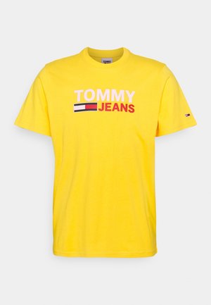 Żółta krótka koszulka z napisem „TOMMY JEANS” i logo flagi nadrukowanymi na piersi oraz małym logo flagi na lewym rękawie.