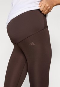 Brune atletiske leggings med en glat tekstur, der har høj talje og tonale logoaccenter. Fremstillet af strækbart, åndbart materiale.