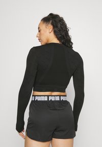 Mustar pikkade varrukatega crop top, millel on tekstuurne muster, kombineeritud mustade lühikesed püksid, millel on valge elastne vöö, millel on "PUMA" logo.
