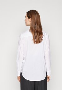 Camicia bianca a maniche lunghe con orlo curvo, polsini abbottonati e dettaglio del giromanica posteriore. Realizzata in tessuto leggero e liscio.