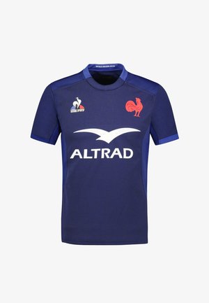 Maillot de sport bleu foncé à manches courtes, avec un logo de poulet rouge et une marque d'entreprise blanche. Fabriqué en tissu léger et texturé.