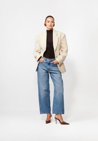 Beżowa żakardowa marynarka na czarnej dopasowanej bluzce, w połączeniu z wysokim stanem niebieskich spodni typu wide-leg i brązowymi szpilkami z ostrym noskiem.