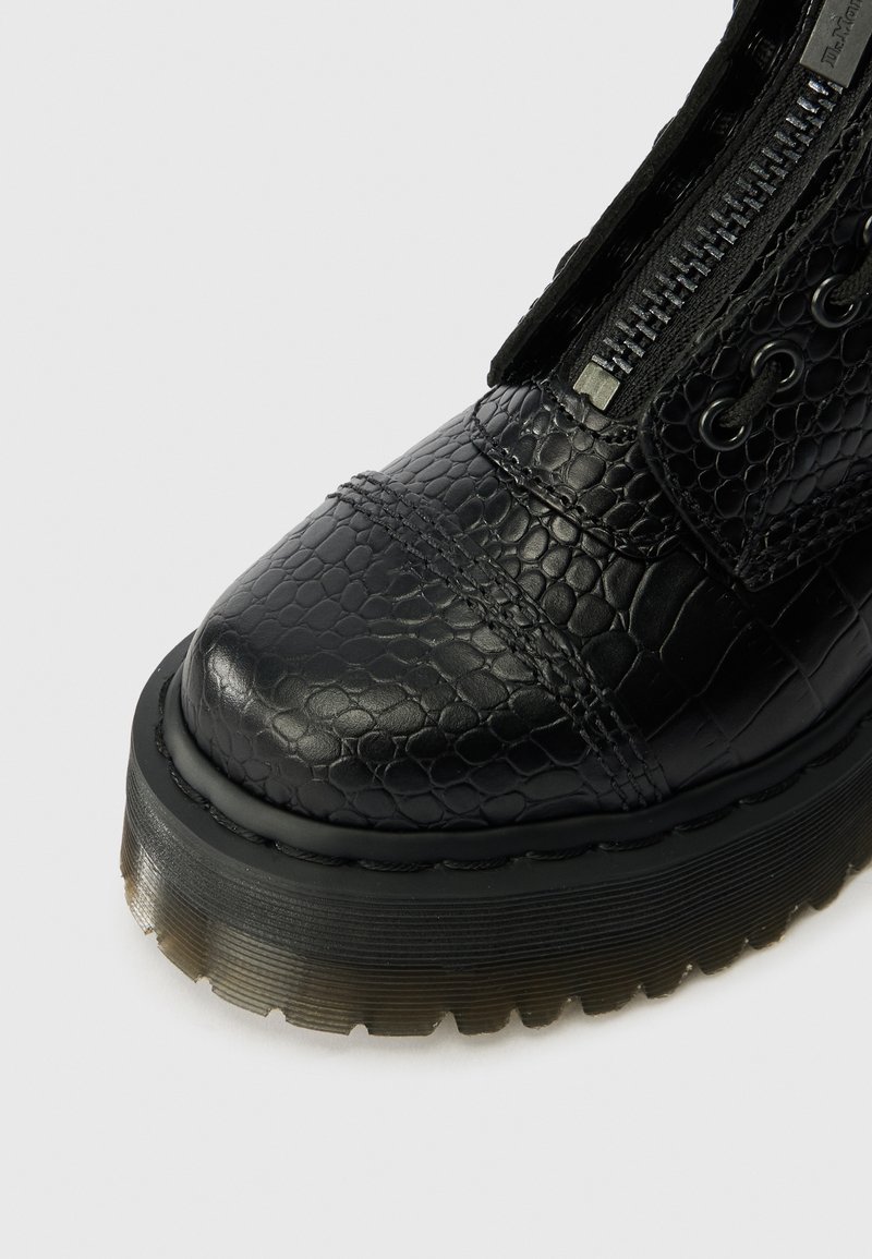 Black leather boot with crocodile texture, thick translucent-ribbed sole, visible zipper, and stitched toe cap detail on white background.