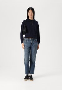 Mornarsko plavi skraćeni pulover s ovratnikom i detaljem s gumbima, u kombinaciji s svijetlim ravnim trapericama i crnim tenisicama s gumiranim potplatom.