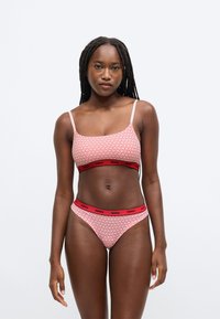 Ružový a biely vzorovaný dvojdielny plavkový set s crop topom s tenkými ramienkami a zodpovedajúcimi vysokými nohavičkami s červeným pásikom s logom značky.