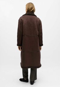 Manteau marron jusqu'aux genoux avec un col et des poignets en fourrure texturée, présentant des détails de couture et un design droit.