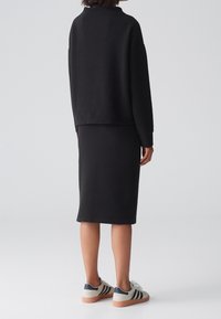 Pull noir texturé à épaules tombantes, associé à une jupe noire ajustée. Chaussures : baskets claires avec des rayures.