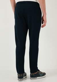 Navy sweatpants van zachte stof, met een elastische taille, taps toelopende benen en een achterzak; gecombineerd met donkere sneakers.