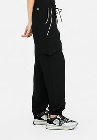 Pantalons cargo larges noirs avec une taille élastique, des poches latérales et des détails en piping blanc. Portés avec des baskets noires et argentées chunky.