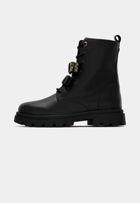Stivale da combattimento in pelle nera con suola spessa e due fibbie decorative, una a fantasia leopardata, vista laterale su sfondo bianco.