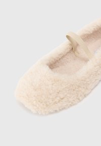 Fuzzy beige ballet flat with a soft, textured upper and a fabric strap. The interior is plush and warm, designed for comfort.