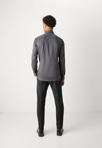 Grijs overhemd met lange mouwen met een lichte glans, manchetten met knopen en een klassieke kraag, gecombineerd met zwarte taps toelopende broek en zwarte schoenen.