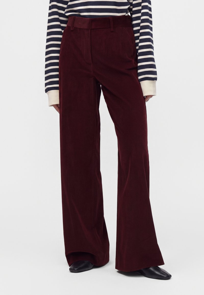 Pantalon en velours côtelé rouge foncé taille haute et jambes larges, porté avec des chaussures noires et un haut à rayures bleu marine et blanc à manches longues.