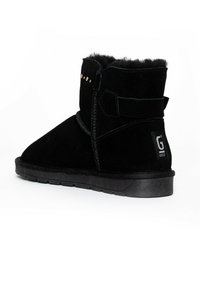 Botines de ante negro con puntera redonda, que presentan una superficie texturizada, tachuelas decorativas doradas y una suela de goma con un logotipo en el talón.