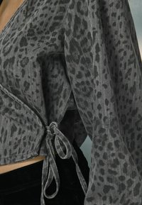 Bluză cu imprimeu leopard gri, dintr-un material ușor, având un design tip wrap și detaliu legat la talie. Finisaj texturat cu mâneci largi.