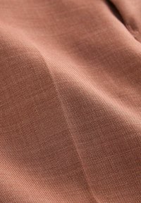 Tissu texturé dans une couleur rose douce, montrant un gros plan de fils entrelacés et d'une surface lisse, mettant en avant son tissage fin.