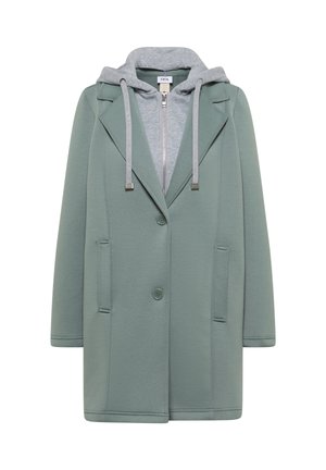 Manteau vert boutonné avec un sweat à capuche gris zippé en dessous, doté de cordons de serrage et de deux poches avant.