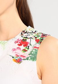 Vestido blanco sin mangas con vibrante bordado floral, con acentos en verde y rojo, y detalles texturizados alrededor del escote.