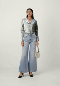 Heledad helesinised laiad teksad, mis on ühendatud hõbedast satiinist pikkade varrukatega särgiga, kus on nööbikinnitus ja krae. Koos valge käekotiga.