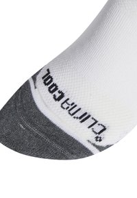 Calcetín de tobillo blanco y gris con tejido texturizado. Secciones de los dedos y el talón en gris, con texto negro a lo largo del borde.