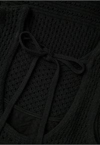 Haut noir en tricot avec une texture en maille, présentant un détail de nœud noué au niveau du cou et une doublure noire solide en dessous.
