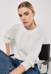 Witte gebreide trui met een textuurpatroon en geribbelde manchetten, met een ronde halsuitsnijding. Draag het met blauwe denim jeans.