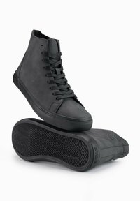 Zapatillas negras de caña alta con un upper de cuero suave, suela de goma texturizada y cordones negros planos. Presentan un diseño minimalista y sin marcas visibles.