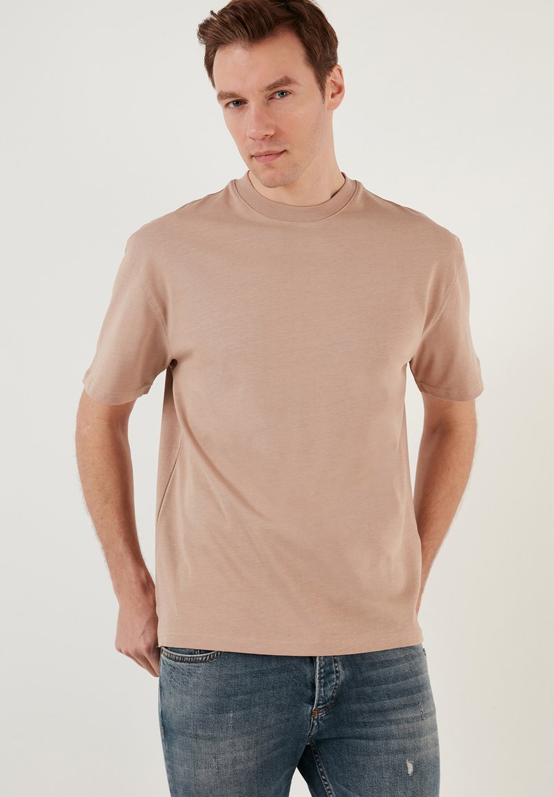 Beige, rövid ujjú, puha pamutból készült póló, kerek nyakkivágással és laza szabással, kék farmernadrággal párosítva.