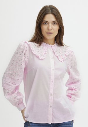 Rožinė bliusonė su broderie anglaise pūstomis rankovėmis, žakardo apykakle ir sagų užsegimu. Minkšta, lengva medžiaga su tekstūriniu akcentu.