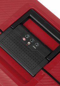 Superficie di una valigia rossa con un motivo texturizzato; presenta un meccanismo di chiusura nero con tre quadranti circolari e uno slot per la chiave.