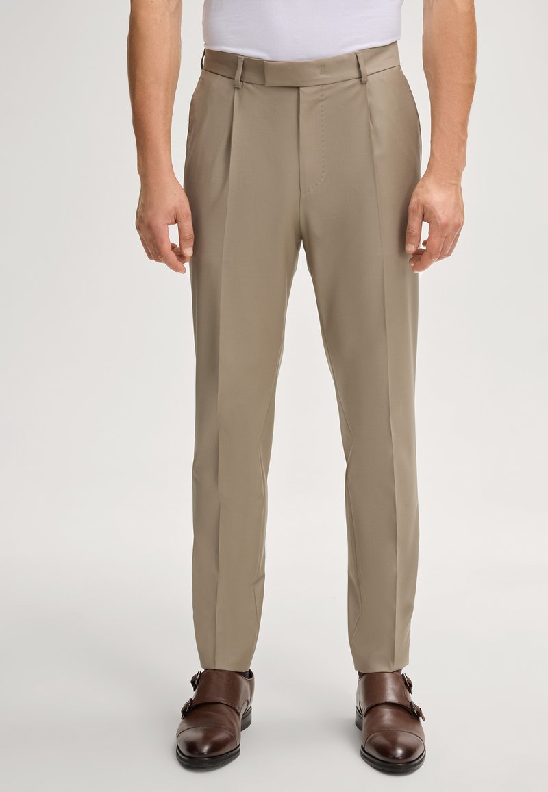 Beige broek met een vlakke voorkant, twee plooien en riemlussen, gecombineerd met bruine leren dubbele monk strap schoenen. Glad stofmateriaal.