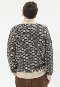 Pletena pulover ima tamnoplavi, svijetlosmeđi i smeđi geometrijski uzorak. Rebrasti ovratnik i manžetne su u boji krem; opušteni kroj s bočnim prorezima.