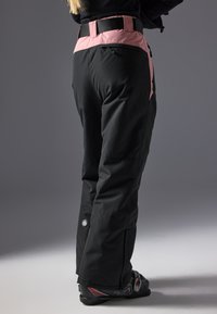 Black ski pants with a pink waistband, featuring a side pocket and a logo patch near the ankle. Made from durable, weather-resistant material.