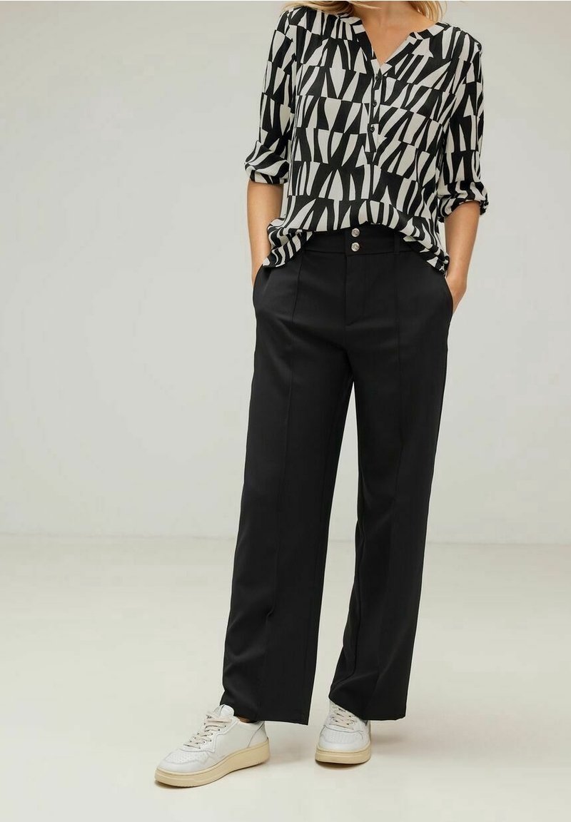 Blusa a righe bianco e nero con maniche arrotolate, abbinata a pantaloni neri dritti e sneakers bianche, con dettagli in bottoni argentati.