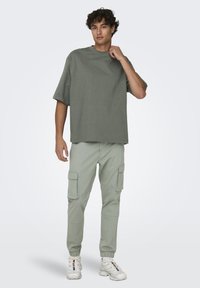 Olijfgroene oversized t-shirt gecombineerd met lichtgroene cargobroek met zijzakken, afgewerkt met witte sneakers.