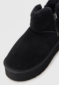 Svarta mockaimitationankelboots med rund tå, dragkedjedetalj och en tjock strukturerad sula, med ett mjukt pälsfoder vid kragen.