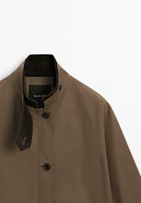 Giacca marrone con colletto alto, chiusura a bottoni e dettaglio testurizzato sul colletto. Realizzata in tessuto liscio, design minimalista senza pattern.