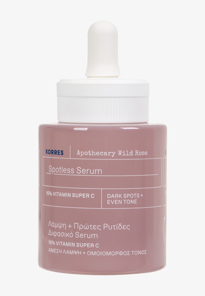 Bottiglia di vetro rosa con tappo contagocce bianco. L'etichetta include "Korres Apothecary Wild Rose Spotless Serum," con testo in inglese e greco.